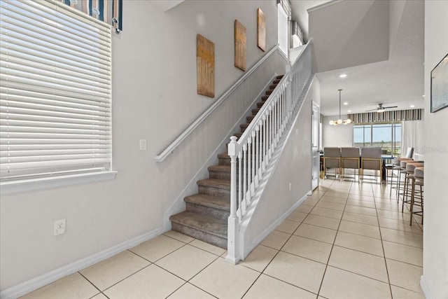 stairs with ceiling fan with notable chandelier and tile patterned floors