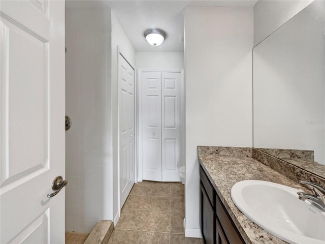 bathroom with tile patterned flooring, a tile shower, a closet, and vanity