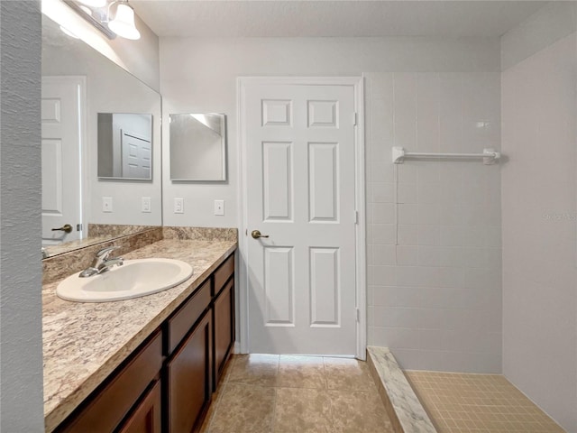 bathroom with tiled shower, tile patterned flooring, and vanity