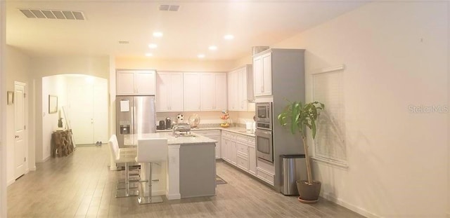 kitchen with stainless steel appliances, light hardwood / wood-style floors, sink, an island with sink, and a kitchen breakfast bar