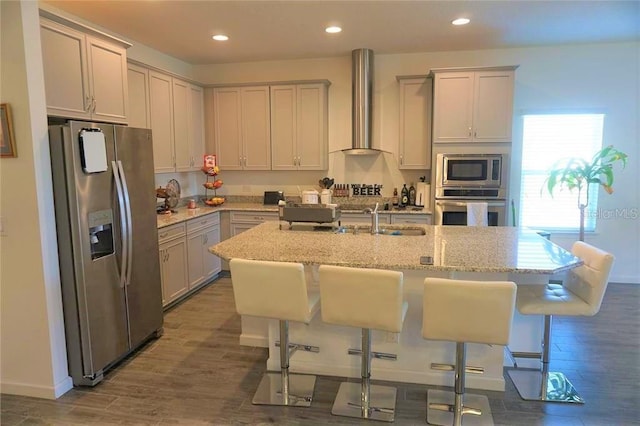 kitchen featuring appliances with stainless steel finishes, a breakfast bar, an island with sink, and wall chimney range hood