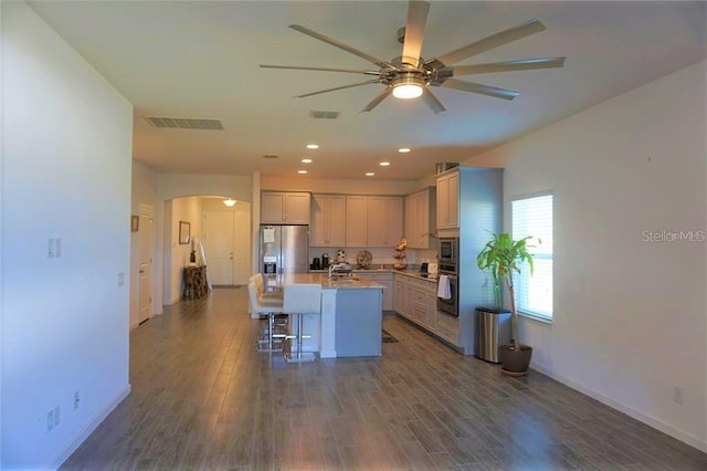 kitchen with dark hardwood / wood-style floors, an island with sink, a breakfast bar, stainless steel appliances, and ceiling fan