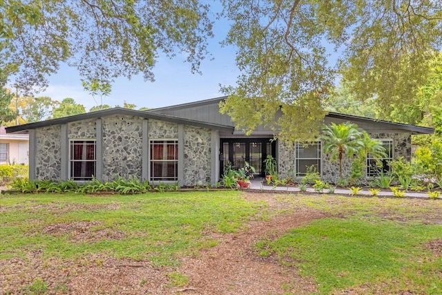 mid-century modern home featuring stone siding and a front yard