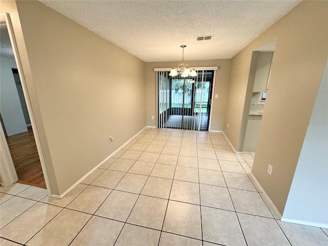 spare room with a textured ceiling, a notable chandelier, and light tile patterned floors