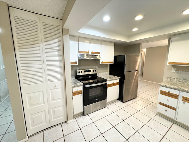 kitchen with a raised ceiling, light tile patterned floors, stainless steel appliances, white cabinetry, and light stone counters