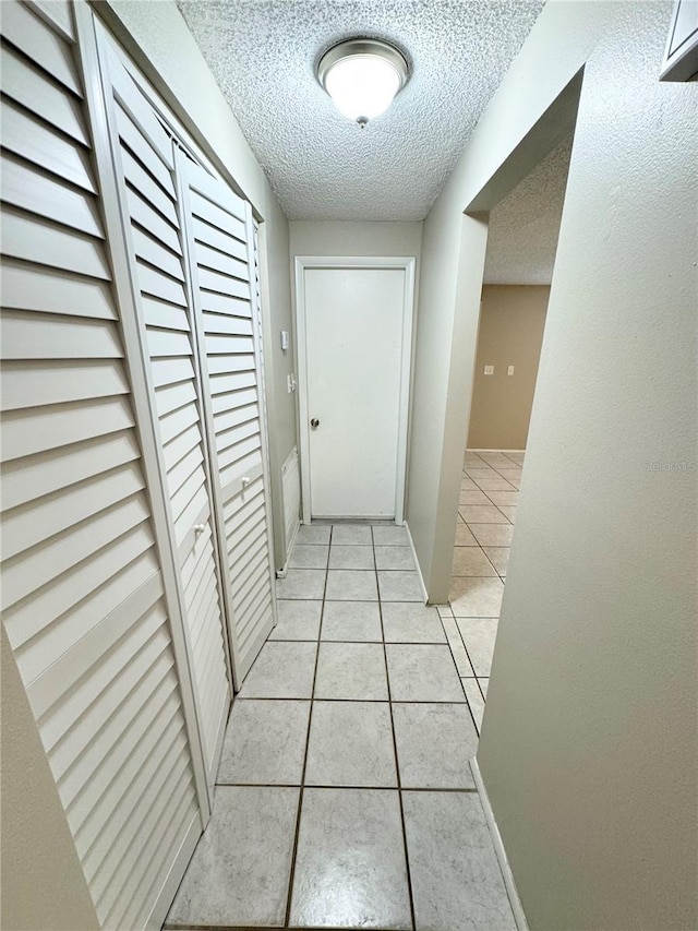 corridor with light tile patterned floors, a textured ceiling, and baseboards