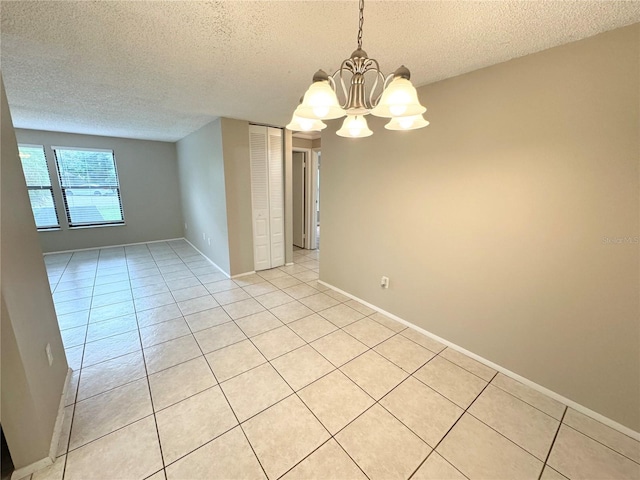 spare room featuring a textured ceiling, light tile patterned floors, baseboards, and a chandelier