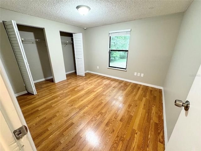 unfurnished bedroom with light wood-type flooring, baseboards, two closets, and a textured ceiling