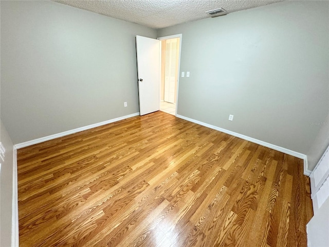 spare room featuring light wood-style flooring, visible vents, baseboards, and a textured ceiling