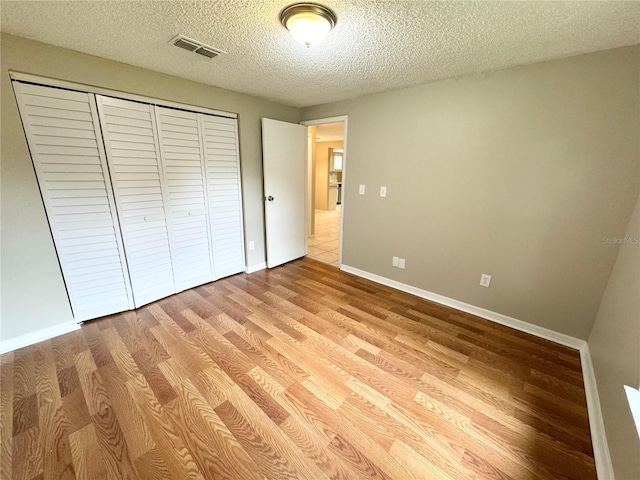 unfurnished bedroom with visible vents, baseboards, light wood-style flooring, a closet, and a textured ceiling