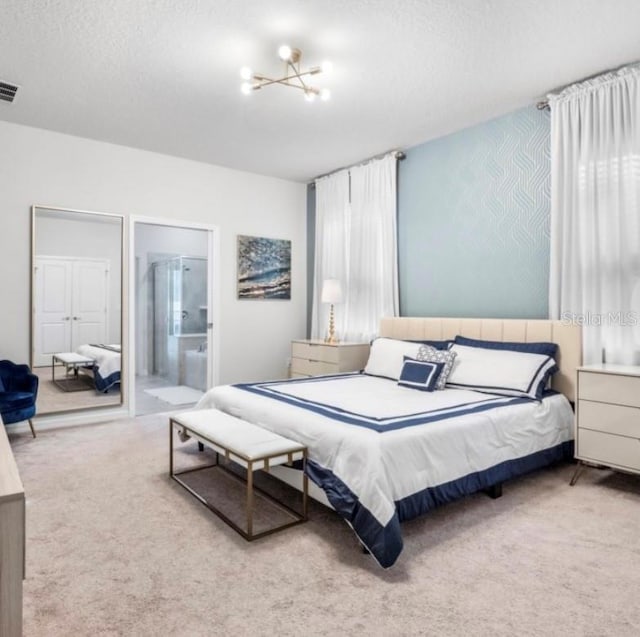 carpeted bedroom featuring an inviting chandelier, a textured ceiling, and ensuite bathroom