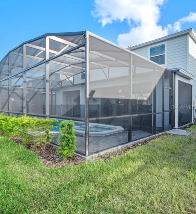 back of house with glass enclosure, a lawn, and an outdoor hot tub