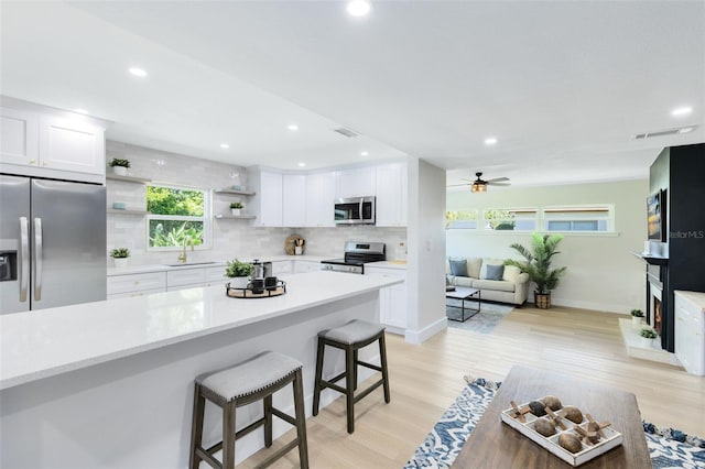 kitchen with a breakfast bar, stainless steel appliances, ceiling fan, and white cabinets