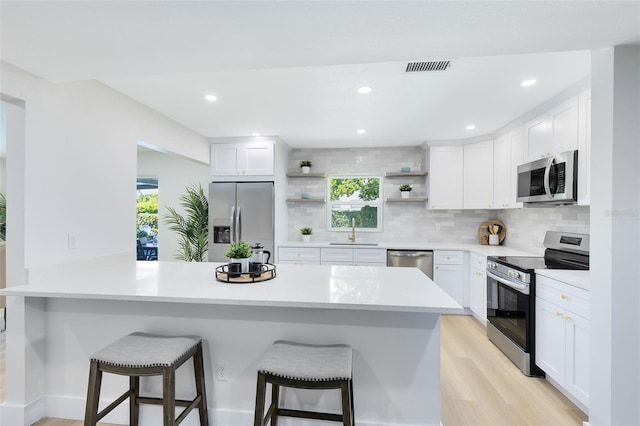 kitchen featuring light hardwood / wood-style flooring, stainless steel appliances, white cabinetry, and a breakfast bar area