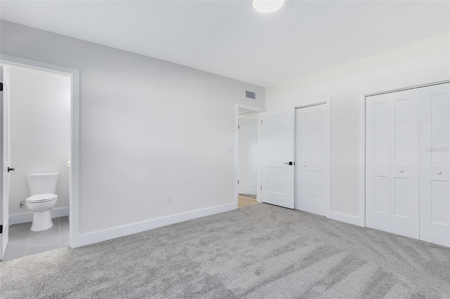 unfurnished bedroom featuring ensuite bath, multiple closets, and light colored carpet