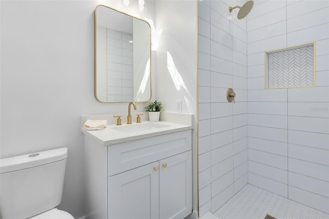 bathroom with toilet, a tile shower, and vanity