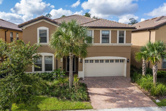 mediterranean / spanish-style home featuring a tiled roof, stucco siding, an attached garage, and decorative driveway