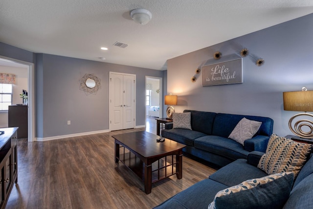 living room featuring visible vents, a textured ceiling, baseboards, and dark wood-style flooring