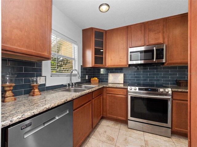 kitchen featuring stone countertops, appliances with stainless steel finishes, tasteful backsplash, sink, and light tile patterned flooring