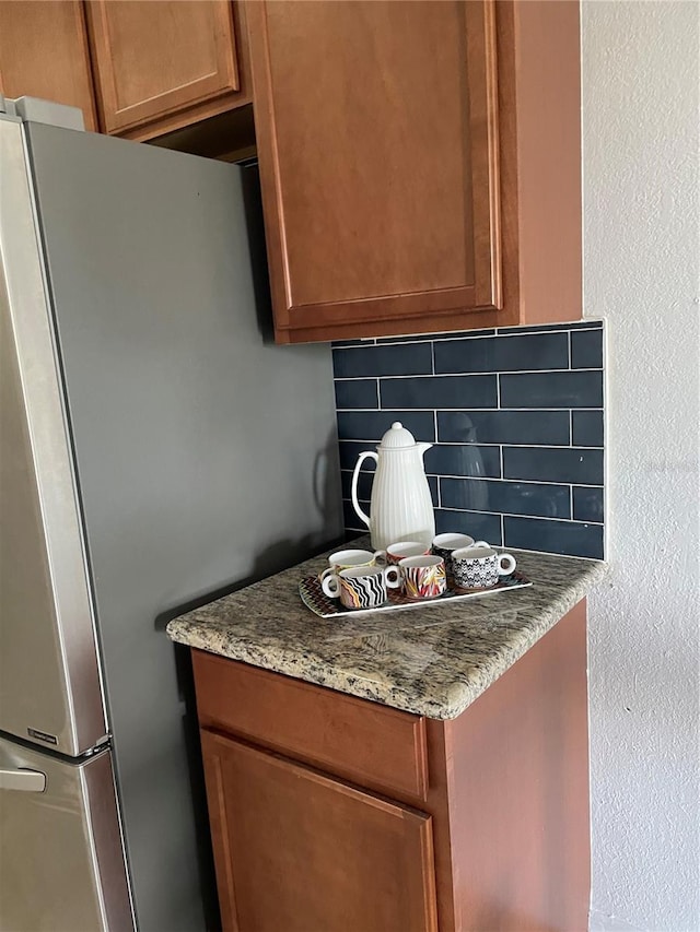 kitchen featuring stainless steel fridge, light stone counters, and tasteful backsplash