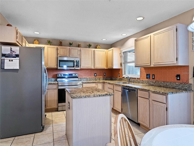 kitchen with appliances with stainless steel finishes, light brown cabinets, light tile patterned floors, a center island, and sink