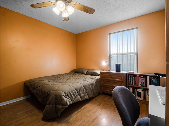 bedroom featuring light hardwood / wood-style flooring, a water view, ceiling fan, and a textured ceiling