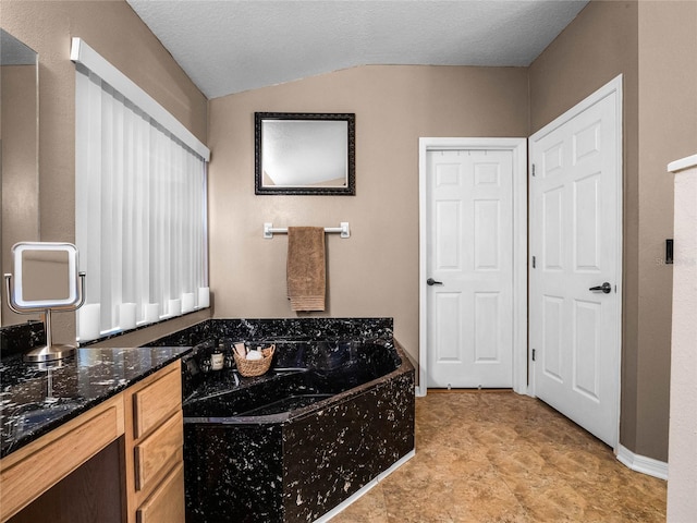 bathroom with lofted ceiling, a textured ceiling, vanity, and a bathing tub