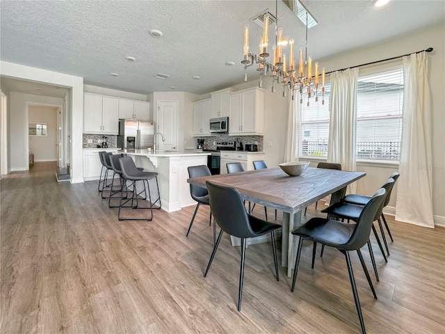 dining room featuring a notable chandelier, light wood-type flooring, a textured ceiling, and sink