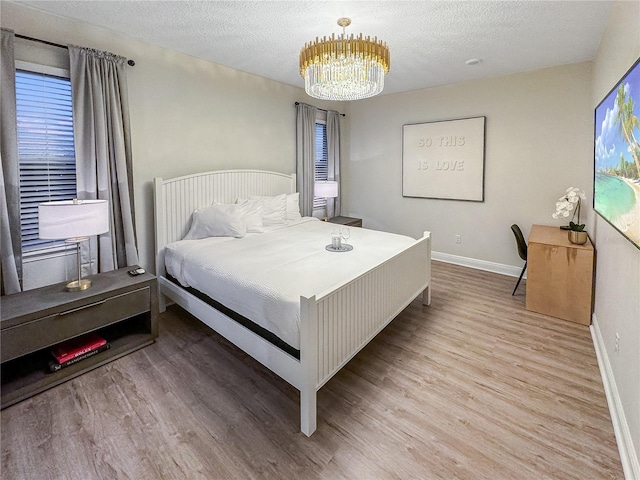 bedroom featuring light wood-type flooring, a chandelier, and a textured ceiling