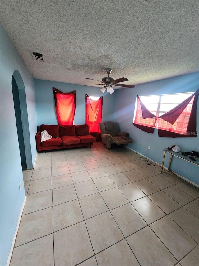 unfurnished living room with ceiling fan, light tile patterned flooring, and a textured ceiling