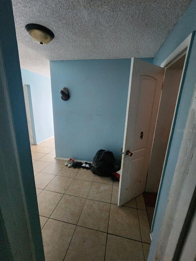 hall with a textured ceiling and light tile patterned floors