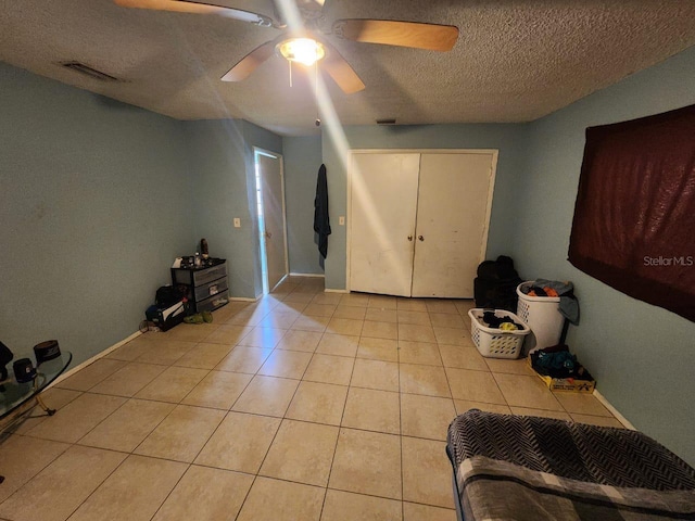 bedroom featuring a textured ceiling, light tile patterned floors, ceiling fan, and a closet