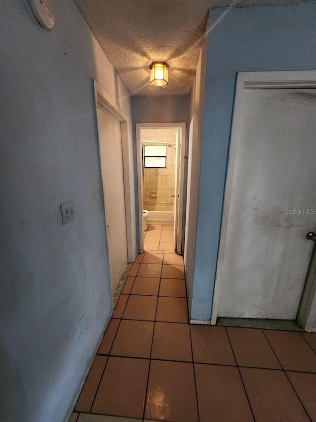 hallway with a textured ceiling and light tile patterned floors