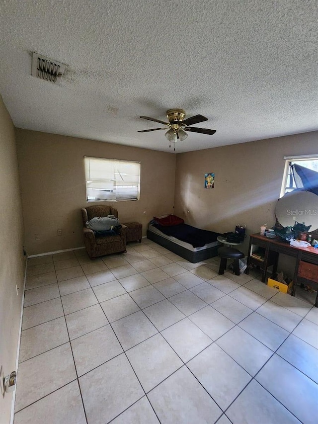 unfurnished bedroom with multiple windows, ceiling fan, light tile patterned floors, and a textured ceiling