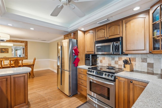 kitchen featuring appliances with stainless steel finishes, light stone counters, light hardwood / wood-style floors, ceiling fan, and ornamental molding