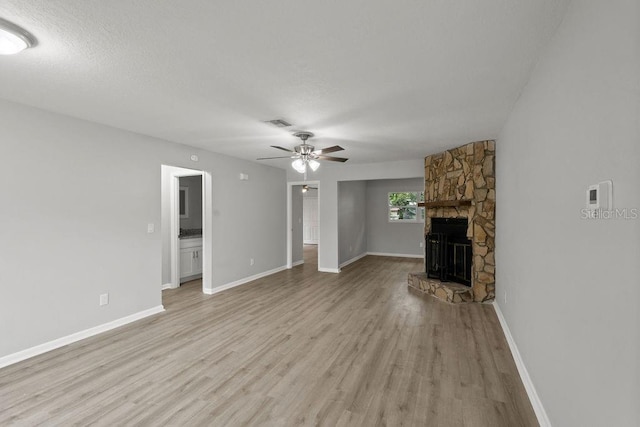 unfurnished living room featuring a fireplace, a textured ceiling, light hardwood / wood-style flooring, and ceiling fan