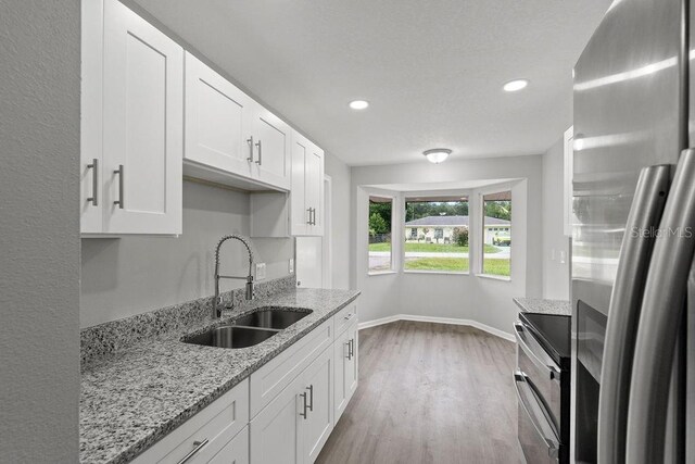 kitchen with light stone countertops, wood-type flooring, stainless steel appliances, sink, and white cabinetry