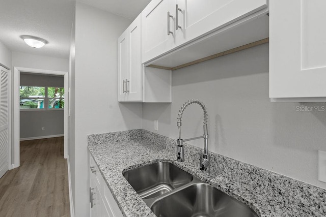 kitchen with light stone counters, sink, white cabinets, and light hardwood / wood-style floors