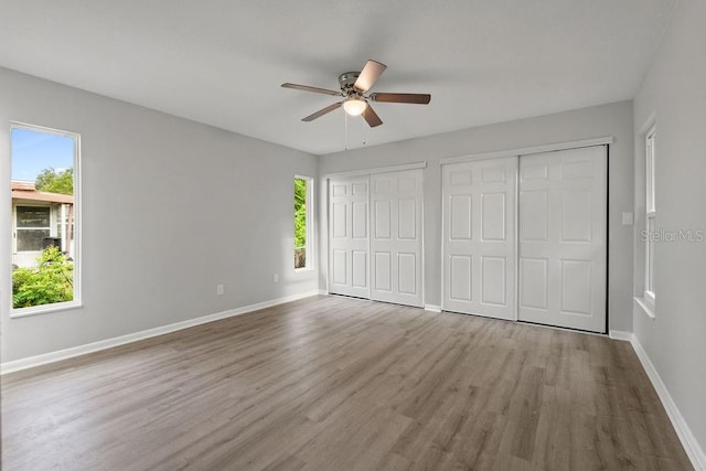 unfurnished bedroom featuring two closets, ceiling fan, and hardwood / wood-style flooring