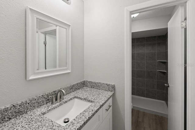 bathroom with wood-type flooring, a tile shower, and vanity