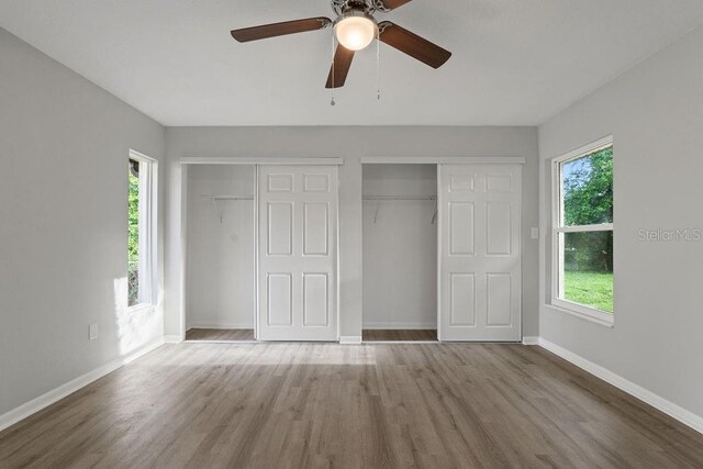 unfurnished bedroom with multiple windows, wood-type flooring, two closets, and ceiling fan