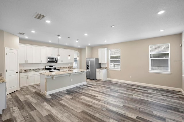 kitchen with appliances with stainless steel finishes, light stone counters, an island with sink, and hanging light fixtures