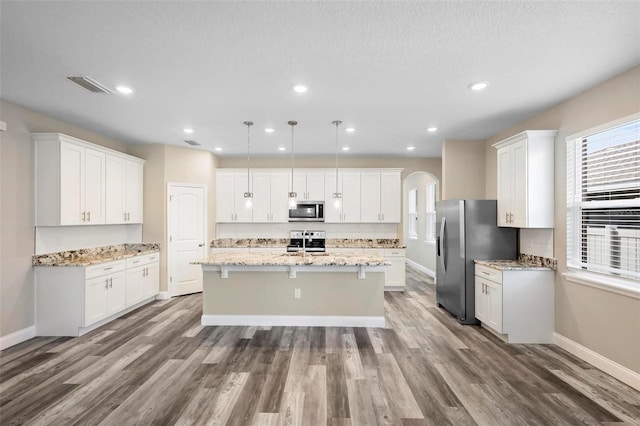 kitchen with a textured ceiling, wood-type flooring, stainless steel appliances, and a center island with sink