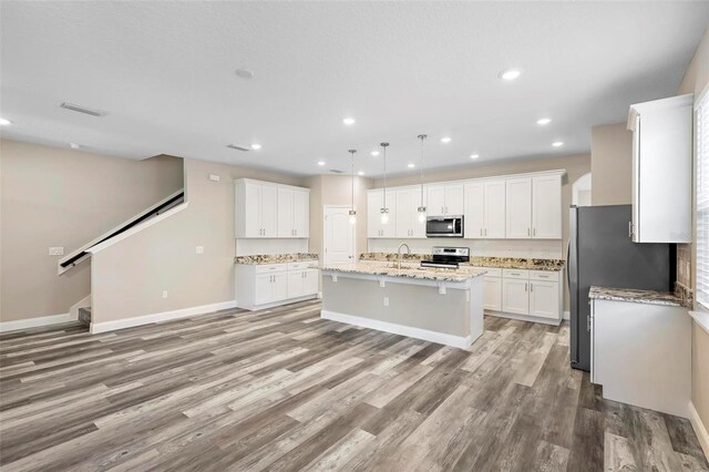 kitchen with hanging light fixtures, stainless steel appliances, white cabinets, and a center island with sink