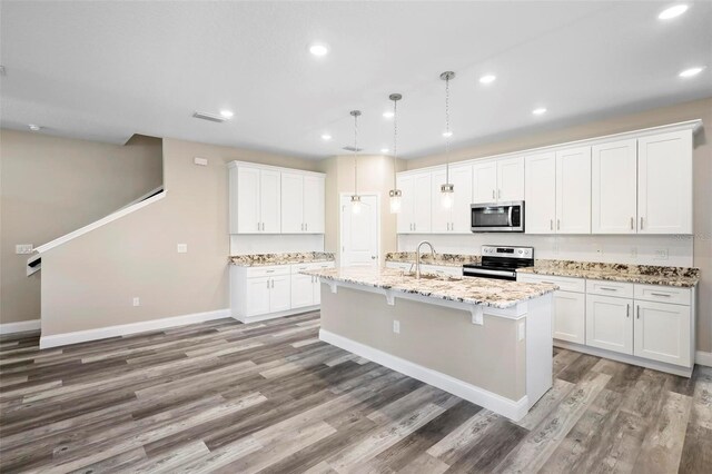 kitchen with a kitchen island with sink, light stone countertops, appliances with stainless steel finishes, hardwood / wood-style flooring, and white cabinets