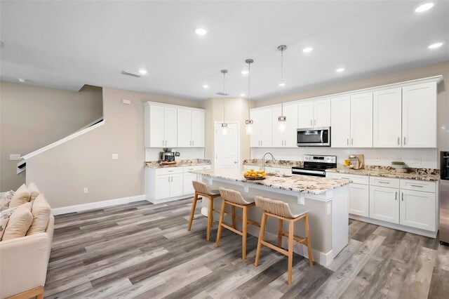 kitchen with an island with sink, appliances with stainless steel finishes, white cabinetry, and light hardwood / wood-style floors