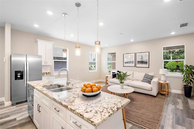 kitchen featuring a healthy amount of sunlight, a center island with sink, white cabinetry, and sink