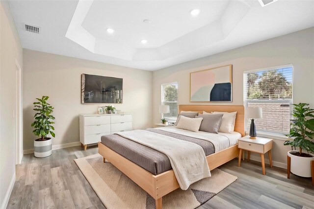 bedroom featuring a tray ceiling, multiple windows, and light hardwood / wood-style floors