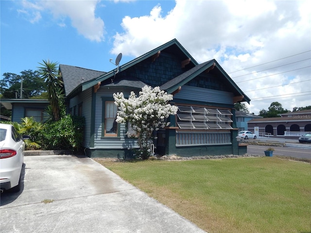 view of front facade with a shingled roof and a front lawn