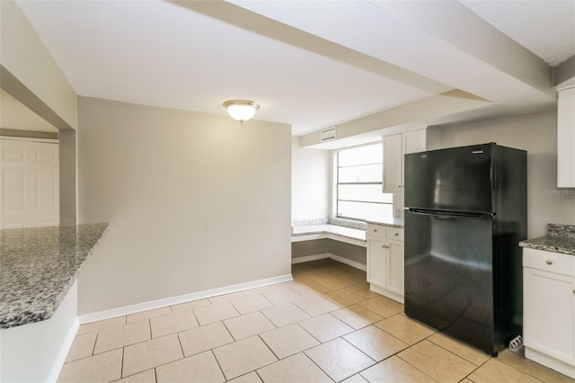 kitchen with baseboards, white cabinetry, light stone countertops, and freestanding refrigerator